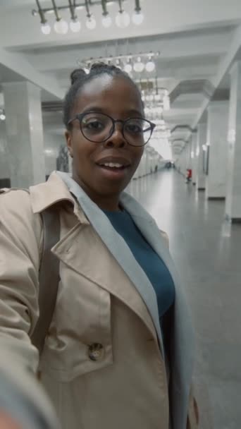 Vertical POV UGC de blogger de viajes afroamericano en gafas y gabardina grabando video contando sobre montar en metro en un nuevo lugar - Imágenes, Vídeo