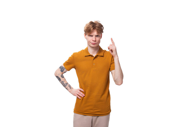 Ένας νεαρός όμορφος κοκκινομάλλης με ένα κούρεμα και ένα τατουάζ στο μπράτσο του λέει τα νέα. έννοια της διαφήμισης. - Φωτογραφία, εικόνα