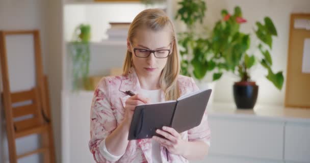 Magabiztos fiatal női vállalkozó írási stratégia naplóba, miközben ott áll a vállalati munkahelyen - Felvétel, videó