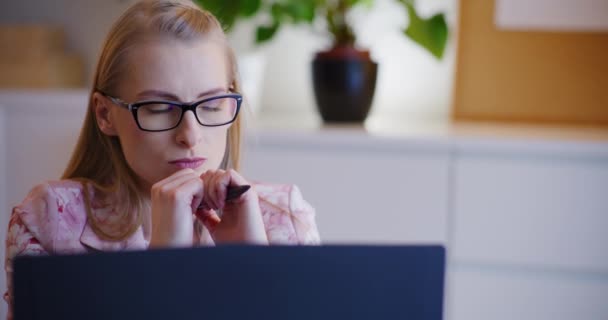 Gözlüklü düşünceli genç iş kadını ofiste dizüstü bilgisayarla oturuyor. - Video, Çekim