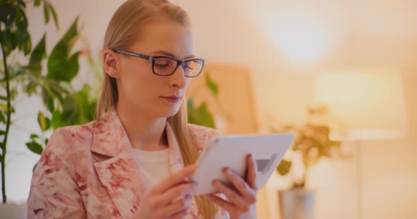Confiante jovem mulher loira profissional vestindo blazer floral navegando na internet em tablet digital no escritório - Filmagem, Vídeo