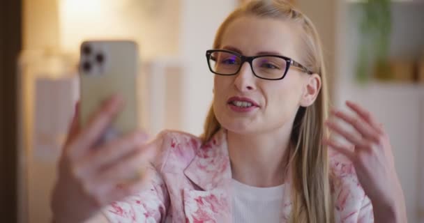 Sonriente joven empresaria gesticulando mientras explica la estrategia de videollamada a través de teléfono inteligente en la oficina - Metraje, vídeo