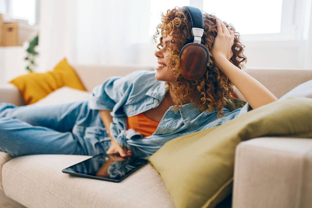 Happy Woman Holding Tablet PC, Élvezi a zenét fejhallgatóval Cozy kanapén otthon - Fotó, kép