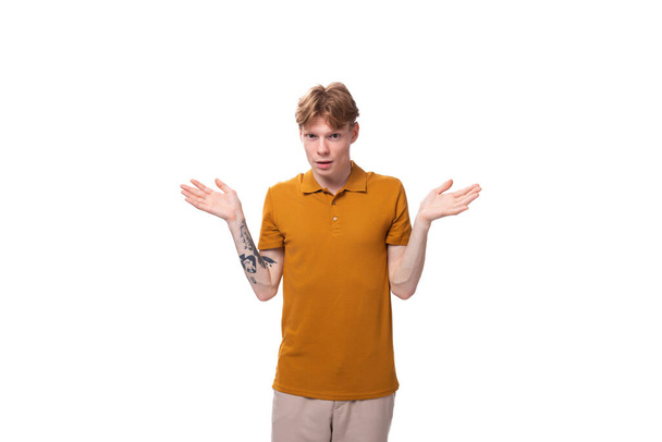 jeune homme roux avec une coupe de cheveux courte et un tatouage sur le bras est habillé d'un t-shirt jaune. - Photo, image