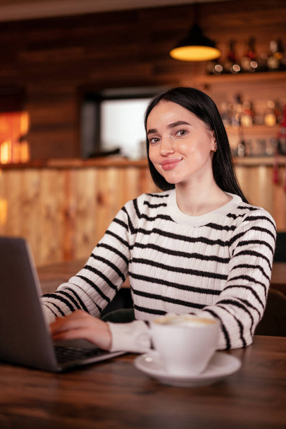 Portrait d'une jolie jeune femme utilisant un ordinateur portable dans un café. Une fille qui travaille sur un ordinateur portable dans un café. Espace de copie - Photo, image