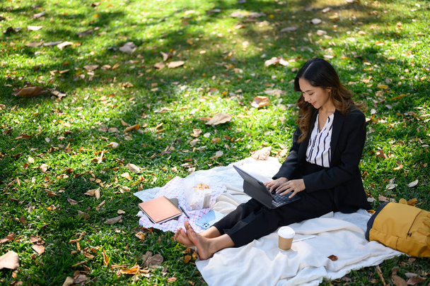 Schöne Geschäftsfrau arbeitet mit digitalem Tablet, sitzt auf grünem Gras im Sommerpark. - Foto, Bild