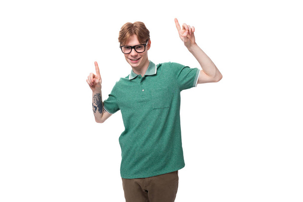 a young man with red hair in a green T-shirt gesticulates joyfully with his hands pointing to the space for advertising. - Photo, Image