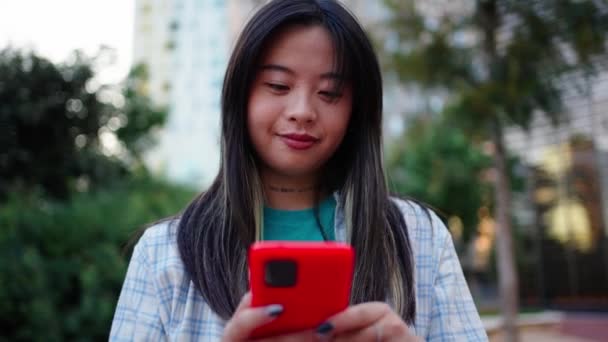 Χαρούμενη Ασιάτισσα που γελάει χρησιμοποιώντας κινητό στην οδό Σίτυ. Generation z Chinese nice female looking happy at mobile screen απολαμβάνοντας περιεχόμενο βίντεο στα μέσα κοινωνικής δικτύωσης. Εθισμένοι στο δίκτυο  - Πλάνα, βίντεο