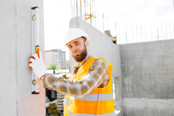 Un muratore-riparatore, caposquadra, in casco protettivo, controlla l'uniformità di una struttura in cemento scale. - Foto, immagini
