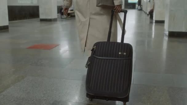 Powrót nachylony obraz niezidentyfikowanej bizneswoman w płaszczu w okopach spacerującej korytarzem z czarną walizką w paski w podziemiu - Materiał filmowy, wideo