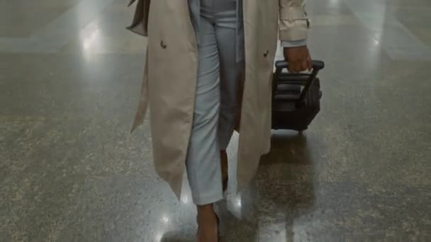 Trençkotlu siyahi bir kadının siyah bavuluyla boş metro lobisinde yürüdüğünü ve telefonda iş konuşması yaptığını görüyorum. - Video, Çekim