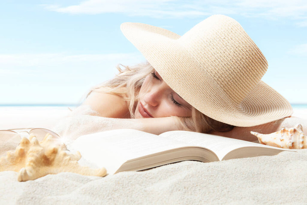 woman lying on sand beach with book, resting wear sun straw hat for sun protection her skin face. Concept of summer beach holiday and vacation travel. Sunglasses, starfish and seashell in foreground - Photo, Image