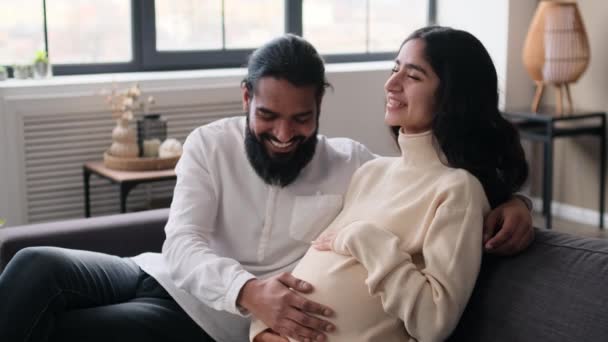 Házas indiai család, feleség és férj, várva a szülést, stroke terhes has otthon, pihentető kanapén. Felkészülés a szülőségre, terhességi idő koncepció. - Felvétel, videó