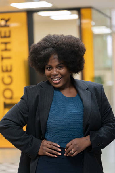 Vrolijke professionele vrouw met afro kapsel in een zakenpak, stralende positiviteit op het werk.  - Foto, afbeelding
