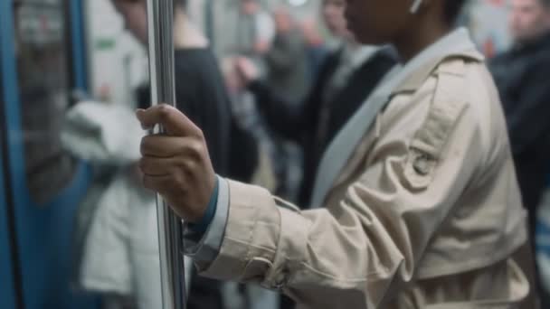 Imágenes recortadas laterales de la señora en gabardina y auriculares sosteniendo mango de poste mientras viaja en metro de transporte público tren al lugar de trabajo - Imágenes, Vídeo