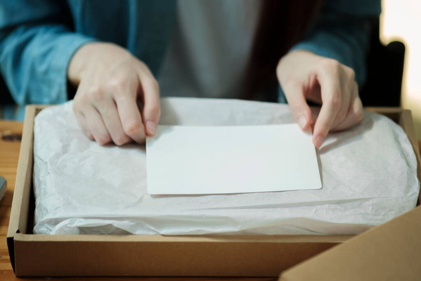 Person preparing a package with a blank card for a custom message. Product packaging and personalization concept. Design for e-commerce, gift wrapping services. - Foto, immagini