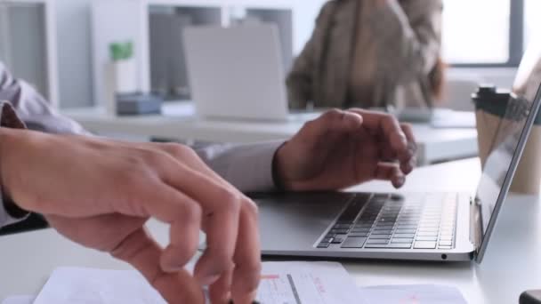 Close-up shot van een Indiase zakenman handen typen op een laptop toetsenbord, schrijven of notities maken in documenten, terwijl het werken in het kantoor aan de balie. - Video