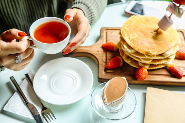 A woman holding a cup of tea and a stack of pancakes on a plate. - Photo, Image