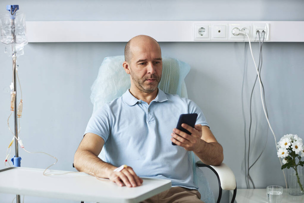 Portrait d'un homme adulte utilisant un smartphone pendant un traitement IV goutte à goutte à l'hôpital, espace de copie - Photo, image