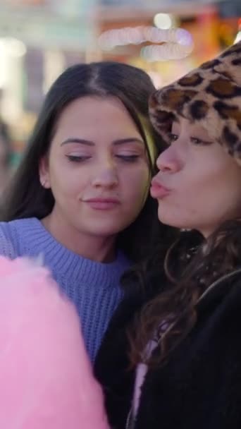 Zwei beste Freundinnen fotografieren gemeinsam auf dem Jahrmarkt in der Nacht Zuckerwatte haltend und lächerliche Gesichter machend - FullHD Vertikales Video - Filmmaterial, Video