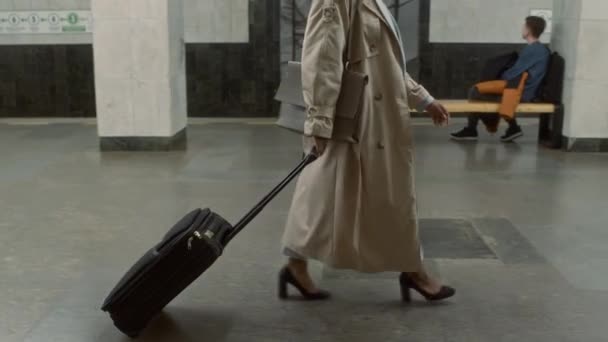 Imágenes laterales de seguimiento completo de una turista afroamericana en viaje de negocios con una maleta negra caminando por un largo pasillo en la moderna estación de metro - Imágenes, Vídeo