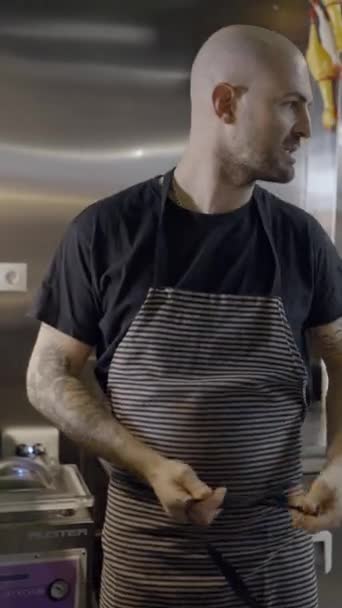 Близкий фронтальный вид лысого шеф-повара, завязывающего фартук на кухне ресторана - FullHD Вертикальное видео - Кадры, видео