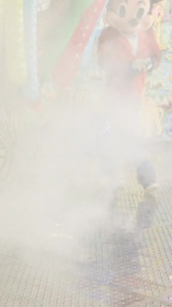 Valencia Kirmes - Mann im Micky-Maus-Kostüm muntert Leute auf, die vorgeben, Haare mit einer großen Schere zu schneiden, wenn Kinder mit dem Zug Achterbahn fahren - FullHD Vertical video - Filmmaterial, Video