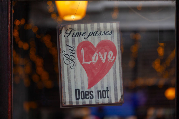 Altes Metallschild im Fenster eines Restaurants mit der Aufschrift: Die Zeit vergeht, aber die Liebe nicht. - Foto, Bild