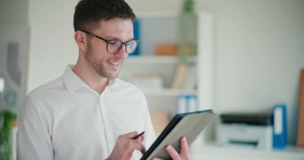 Usmívající se mladý podnikatel pomocí digitálního tabletu, zatímco stojí na firemním pracovišti - Záběry, video