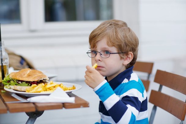 mały chłopiec, jedzenie fast food: hamburger i frytki - Zdjęcie, obraz
