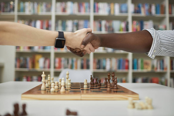 Zijaanzicht close-up van twee schaakspelers die elkaar de hand schudden over schaakbord na wedstrijd - Foto, afbeelding