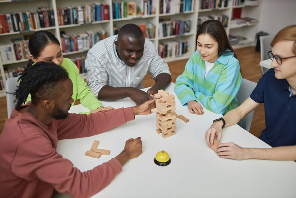 High angle view at diverse group of friends enjoying game of balance tower in library - Fotó, kép