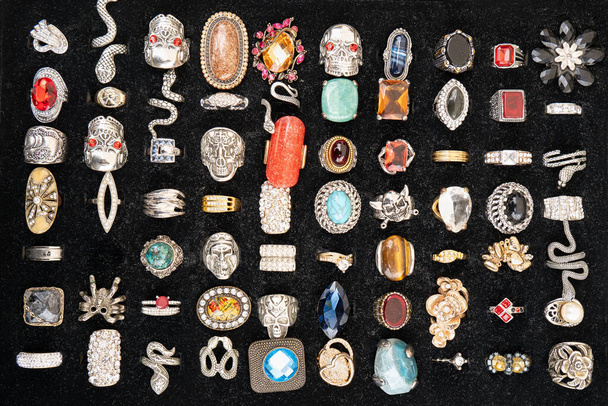 Um monte de anéis desgastados e anéis de pedra preciosa de várias formas no fundo preto que vende em um mercado de pulgas - Foto, Imagem