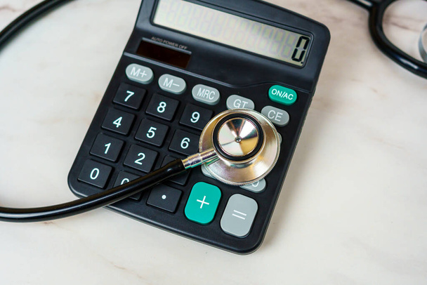 Stéthoscope et calculatrice sur table. Frais médicaux, frais de santé, fardeau financier de la maladie - Photo, image