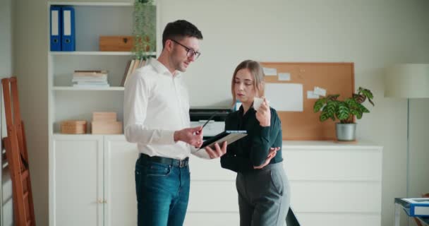 Young businessman showing strategy on digital tablet to businesswoman drinking coffee while standing in office - Footage, Video