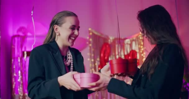 Boldog fiatal női barátok cseréje ajándékdobozok alatt Galentine napi ünneplés lakásban - Felvétel, videó