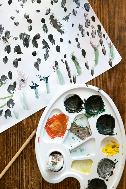 Uma paleta suja para misturar aquarelas. Na mesa - uma folha de papel pintada e uma escova. O conceito de arte e hobbies para crianças - Foto, Imagem