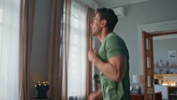 Energetic sportsman exercising at home close up. Enthusiastic young man jumping making cardio exercises in modern living room. Handsome muscular guy have active morning workout in apartment interior. - Footage, Video