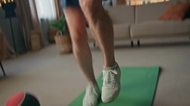 Sportlerfüße springen aktiv auf sportlichen Matten zu Hause Nahaufnahme. Starker junger Mann trainiert im Wohnzimmer gesunden Körper. Motivierte, gut aussehende Athletin wärmt sich vor dem täglichen Training in der Wohnung auf - Filmmaterial, Video