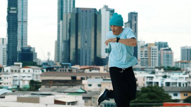 Dançarino B-boy caucasiano experiente praticando dança de rua no telhado com locais da cidade ou urbano. Filmagem do jovem realizando dança de rua fazendo pose de congelamento. Desporto ao ar livre 2024. Endeavor. - Foto, Imagem