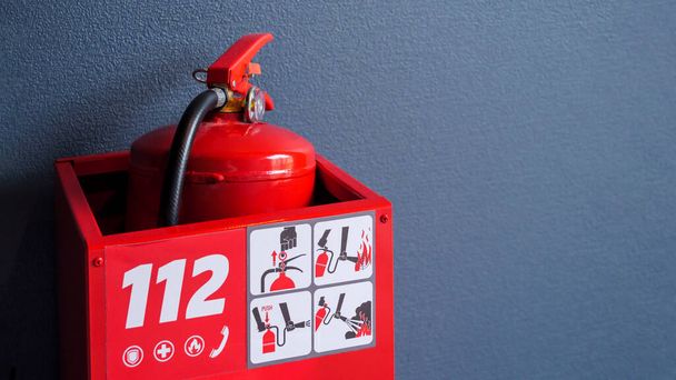 Ένας κατακόκκινος πυροσβεστήρας αποθηκεύεται μέσα σε ένα κόκκινο κουτί με τον αριθμό έκτακτης ανάγκης 112 και οδηγίες χρήσης. - Φωτογραφία, εικόνα
