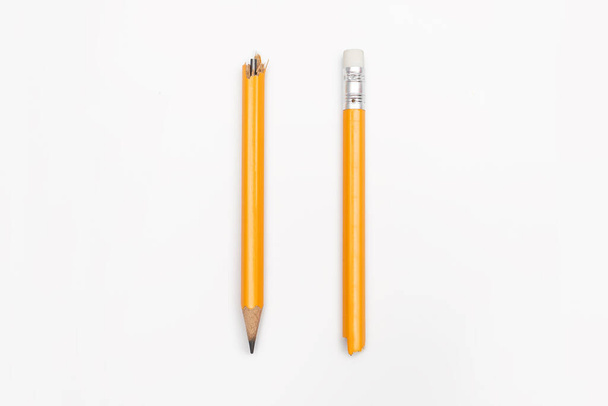 Сломанный карандаш вертикально расположен на белом горизонтальном фоне. Желтый графитовый карандаш разбит на две половины крупным планом. Эмоции, стресс, агрессия, проблемы в учебе, проблемы на работе. - Фото, изображение