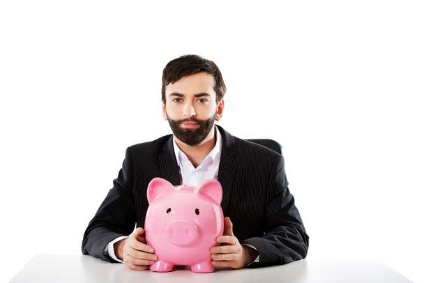 Businessman with piggybank by a desk. - Foto, Bild