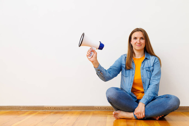 Alkalmi fiatal nő kezében egy megafon, miközben ül keresztbe tett lábakkal egy fapadlón, koncepció kommunikáció. - Fotó, kép