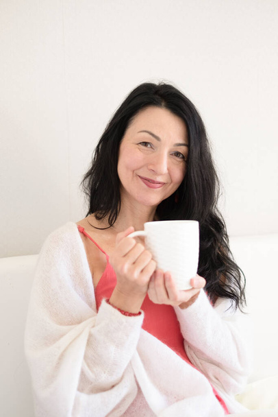 Uma mulher serena isolada com cabelo preto está desfrutando de uma bebida quente, incorporando a aceitação calma das alterações hormonais da meia-idade e da menopausa. Foto de alta qualidade - Foto, Imagem