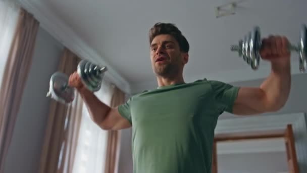 Güçlü vücut geliştirici sabah evde egzersiz yaparken dambılı kaldırıyor. Apartman dairesinde güçlü eller eğitimi alan yakışıklı bir adam. Sağlıklı vücut için kaslarını çalıştıran odaklanmış bir sporcu.. - Video, Çekim