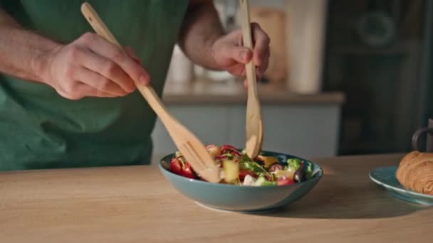 Erkek elleri, ev mutfağında salatayı karıştırıyor. Bilinmeyen bir erkek, sağlıklı yemek hazırlıyor. Genç adam elinde tahta spatula tutarak yemek yapıyor. Vejetaryen beslenme konsepti  - Video, Çekim