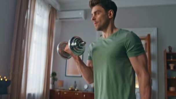 Svalový atlet trénink biceps v bytě obývací pokoj zblízka. Vážný motivovaný muž zvedá činky pro silné ruce doma. Fešák sportovní cvičení s vybavením uvnitř. - Záběry, video