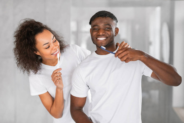 Loving married african american couple brushes teeth together, smiling while enjoying shared toothcare and love in the bathroom. Wellness in daily routine of young family - Photo, Image