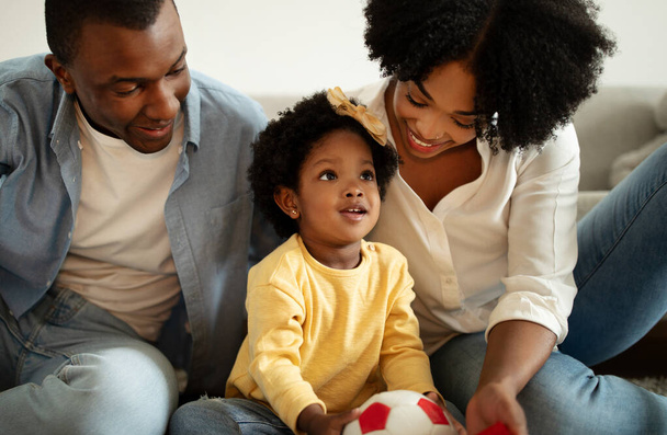 Tudatos nevelés. Az afro-amerikai család apjának, anyjának és kisgyermekének közelsége, akik otthon élvezik az együtt töltött időt. Boldog szerető fekete szülők játszanak a kislányukkal. - Fotó, kép
